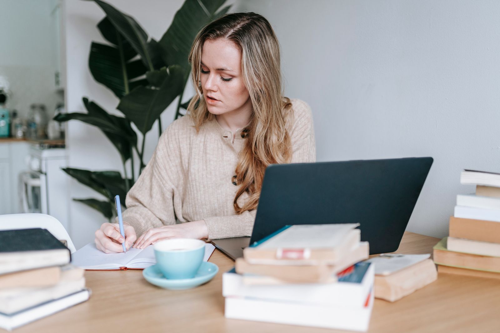 Businesswoman writing notes in a notebook next to a laptop and coffee