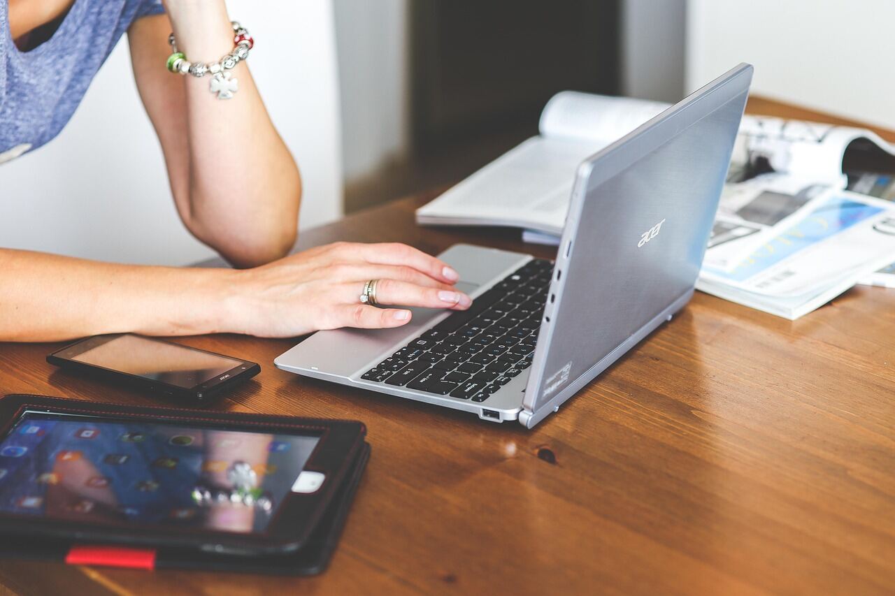Person working on a laptop at a warm wooden desk with a phone and tablet nearby, keeping a website up to date