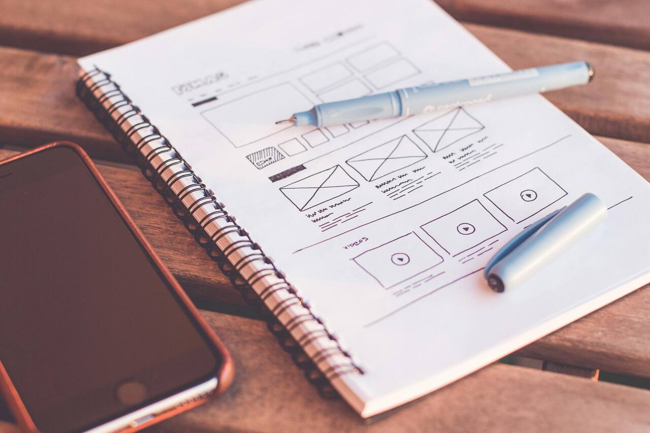 Notebook of website wireframe sketches beside a phone