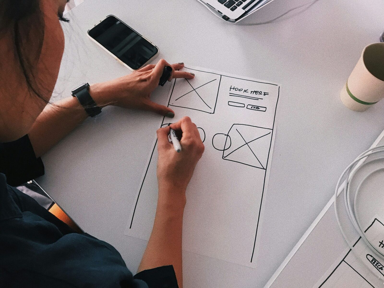 Designer sketching a website wireframe on paper with hook section, CTA, and content blocks — planning a clearer page structure as part of a website redesign for NZ small businesses